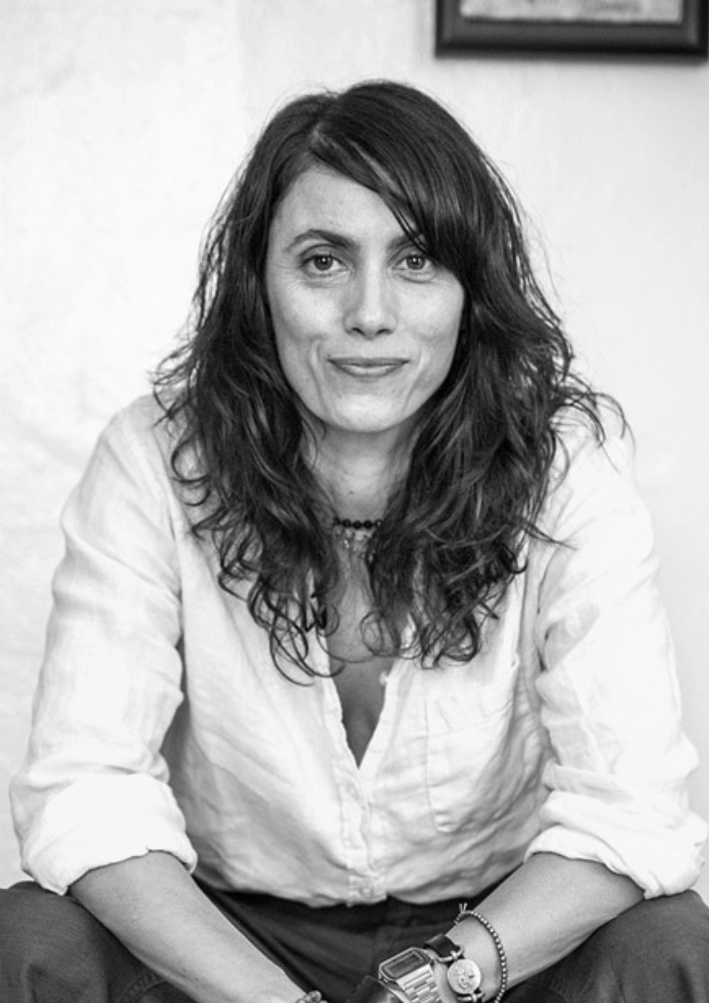 A black and white portrait of a woman with long, wavy hair wearing a white button-down shirt.
